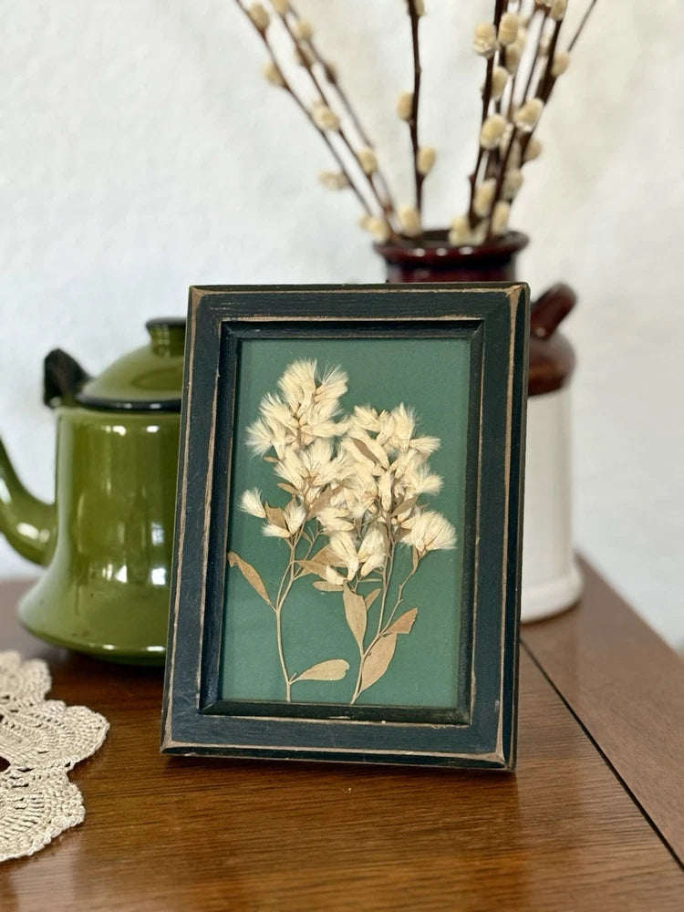 Framed under-glass dried flower print with pale beige blooms and dark teal frame