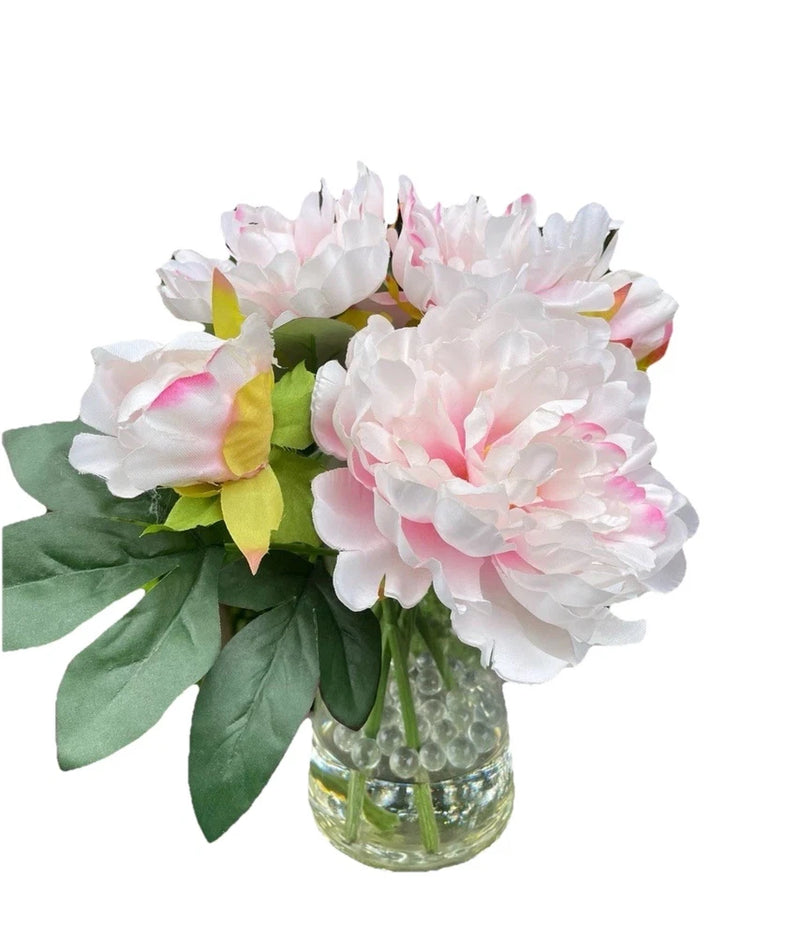 Light pink silk peony flower bouquet with green leaves in clear glass vase