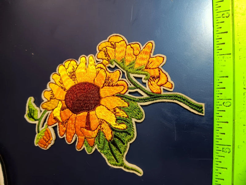 Embroidered sunflower flower patch with yellow petals and green leaves, close-up