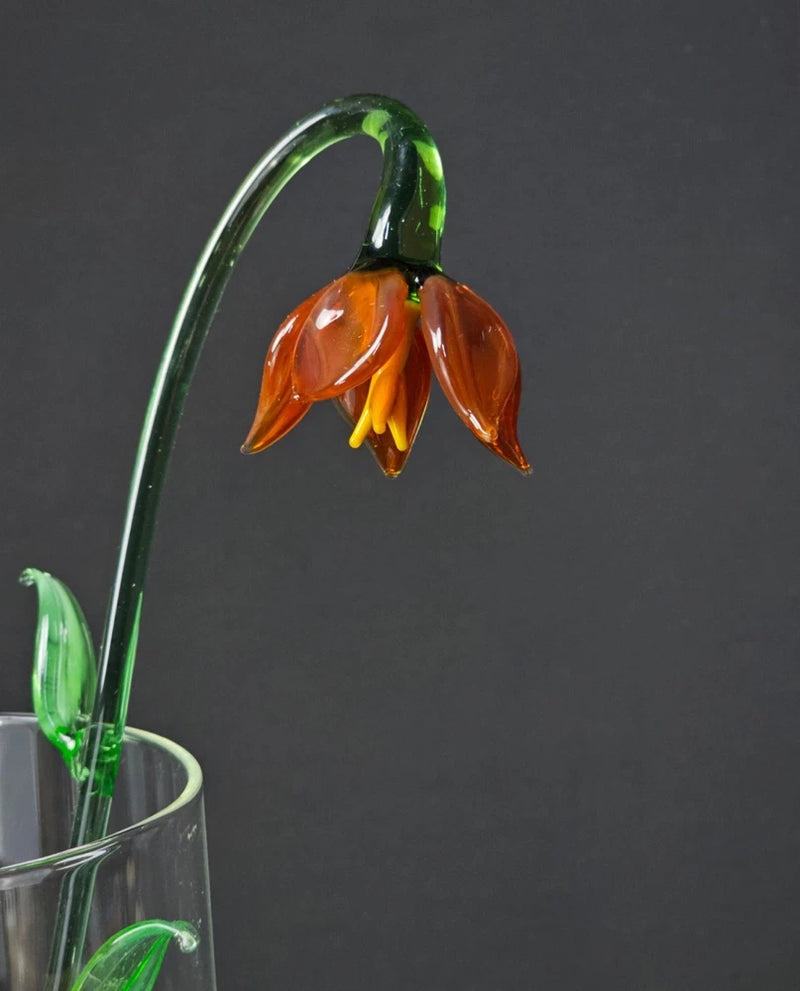 Amber orange glass lily flower with green stem and yellow center