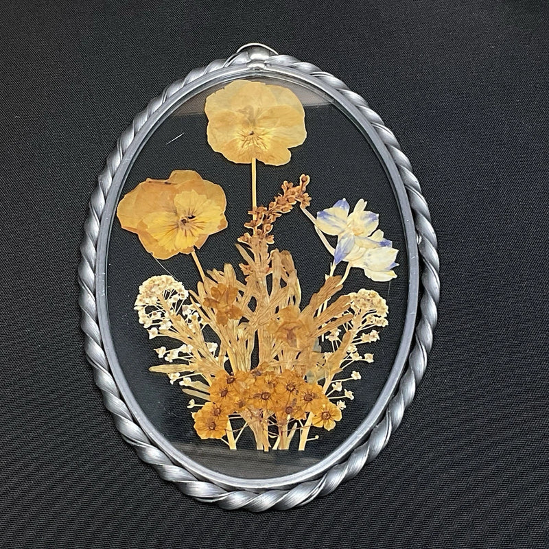 Oval glass metal frame with pressed dried flowers in yellow and tan