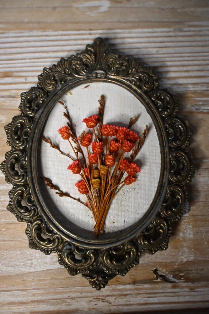 Small oval framed dried flower arrangement with orange blooms in vintage ornate frame
