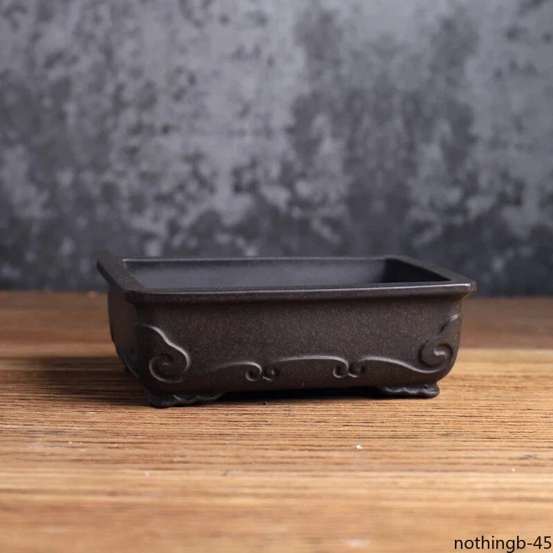 Small dark ceramic flower pot with scalloped rim and decorative scroll feet