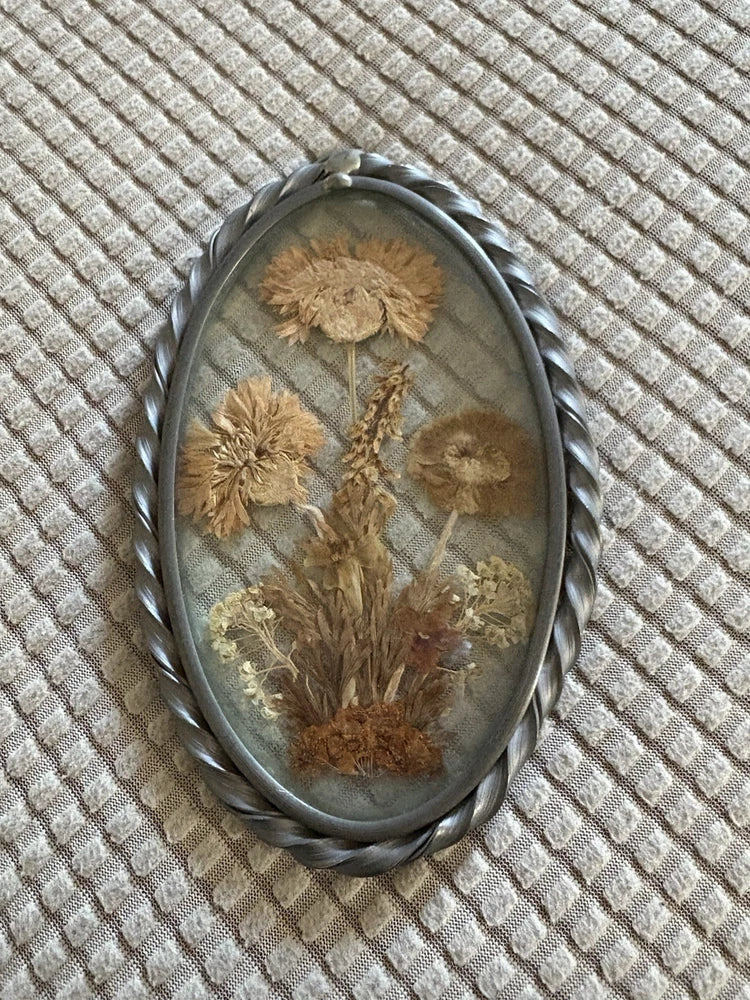Oval glass framed dried flowers in twisted metal hanging frame