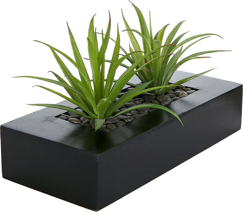 Artificial grass plant in black rectangular planter with faux green blades and pebbles