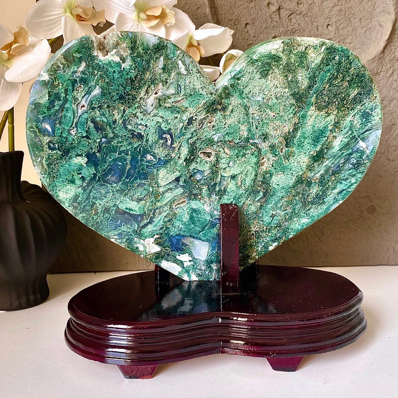 Heart-shaped green crystal specimen on dark wooden base