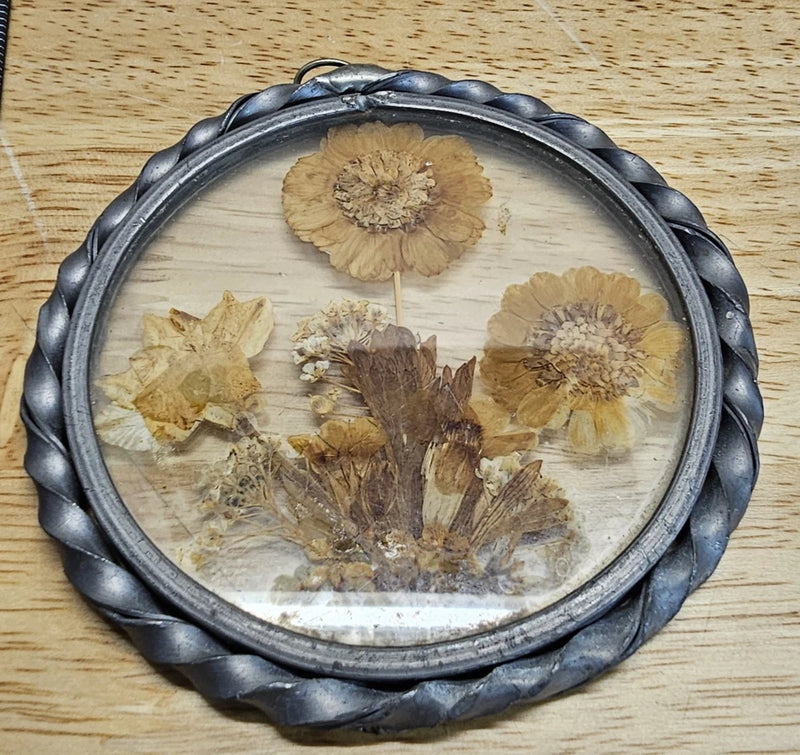 Oval glass hanging frame with dark metal border and pressed dried flowers bouquet
