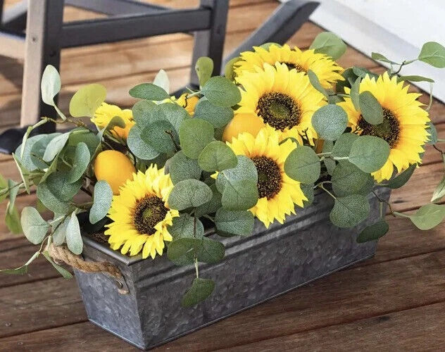 Faux sunflower and eucalyptus floral arrangement in dark rectangular planter with yellow blooms