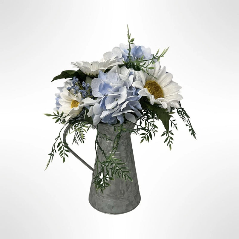 Galvanized metal pitcher floral arrangement with blue and white blooms and green leaves