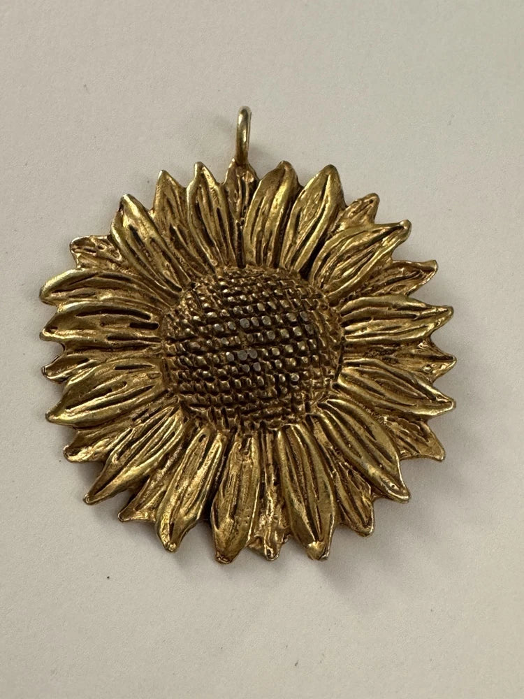 Gold-tone sunflower pendant with textured petals and raised center, hanging loop on top