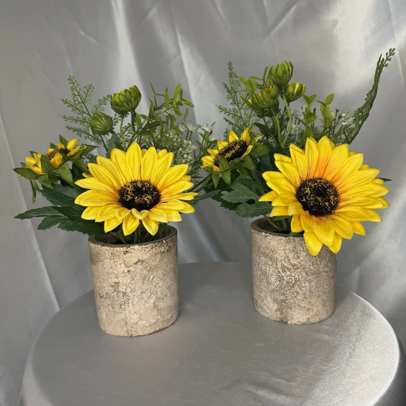 Two small artificial sunflower blooms in gray textured pots with green leaves