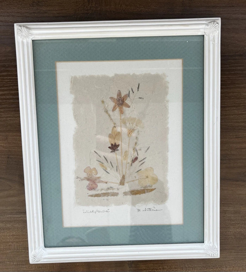 Framed pressed dried flower artwork with wildflower stems and scattered petals