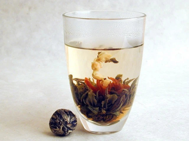 Blooming flower tea in clear glass with floating dried petals and buds