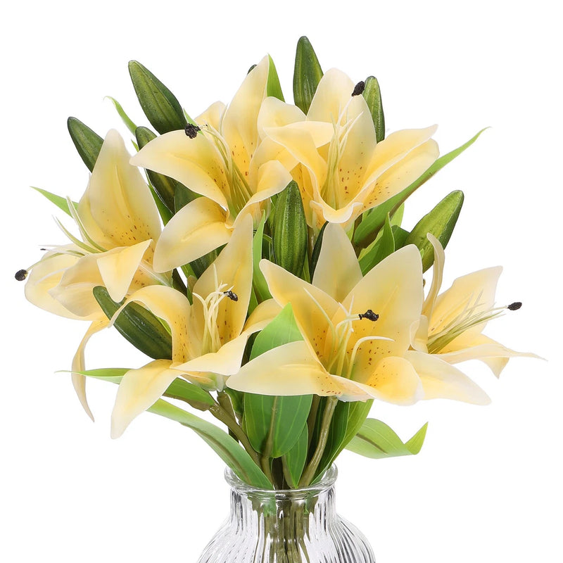 Artificial yellow lily flower bunch with green leaves in clear glass vase