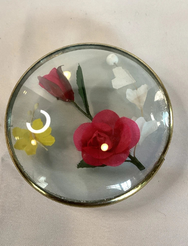 Circular glass frame with red faux flower and green leaves, plus small yellow blooms