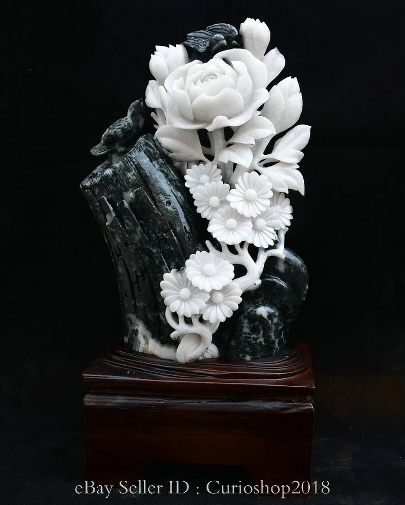 Jade carving flower bird statue with white blossoms on dark stone base, on wooden stand