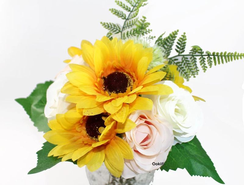 Artificial flower bouquet with yellow sunflower heads, white and pink roses, green leaves and greenery