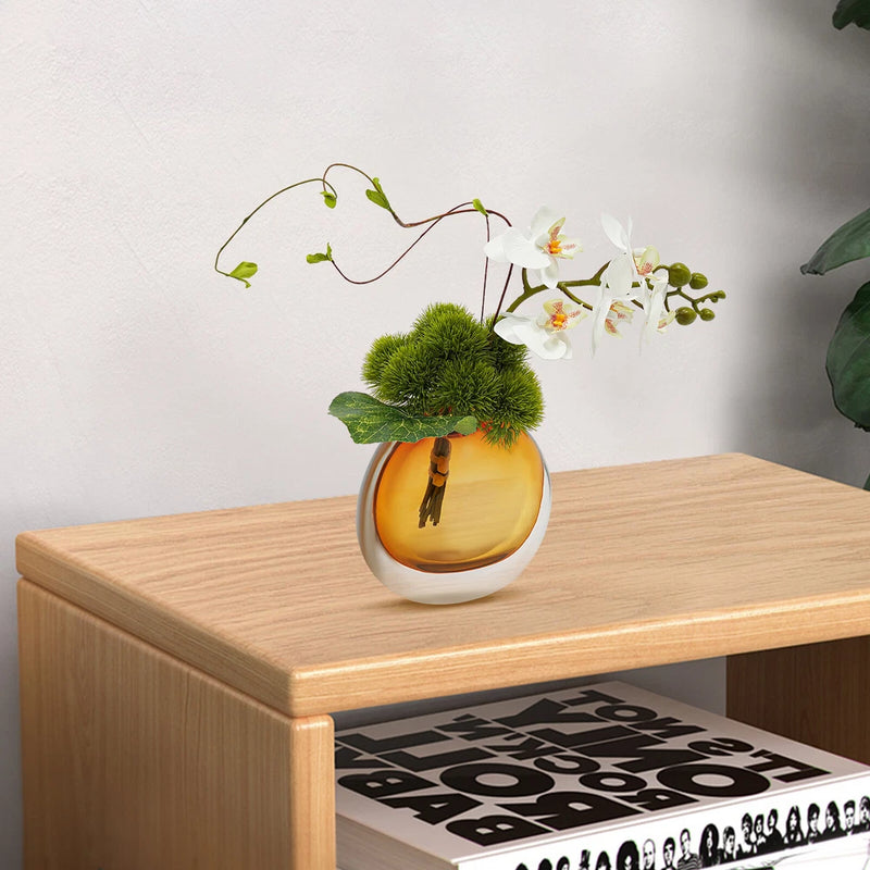 Artificial flower arrangement in a round vase with white blossoms and green foliage