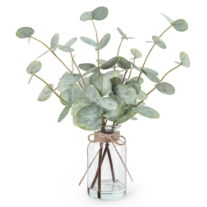 Artificial eucalyptus stems in clear glass vase with faux water and green leaves