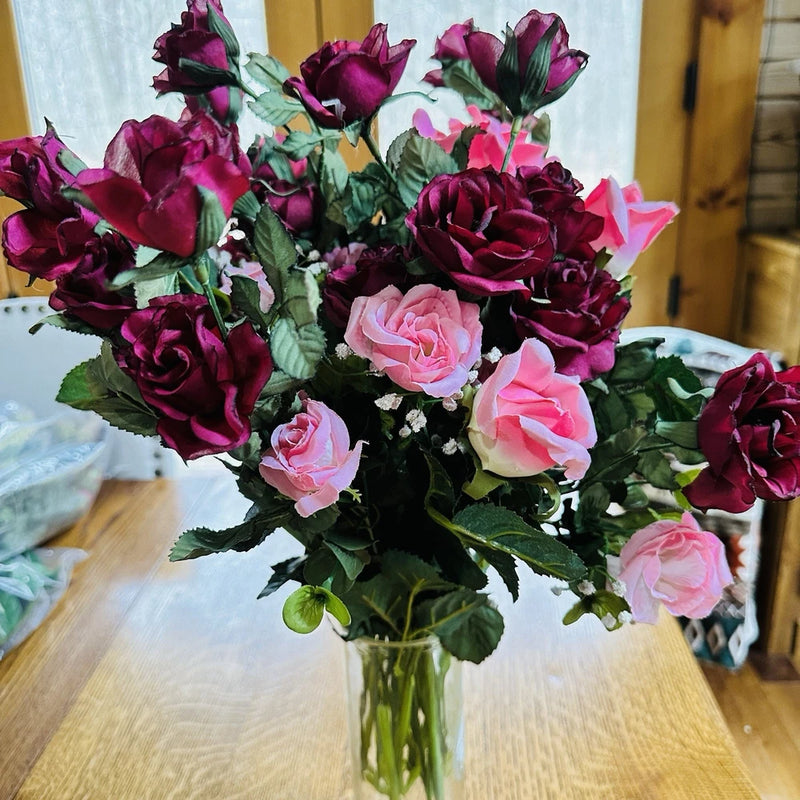 Artificial rose bouquet with burgundy and pink blooms, green leaves, in clear vase