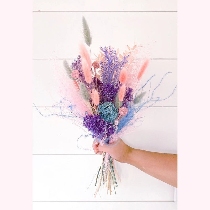 Dried flower bouquet with purple and pink blooms, blue filler, and grasses, held by hand