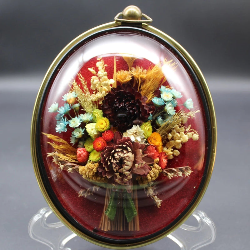 Oval brass-framed domed glass dried flower bouquet with pinecones and red backing