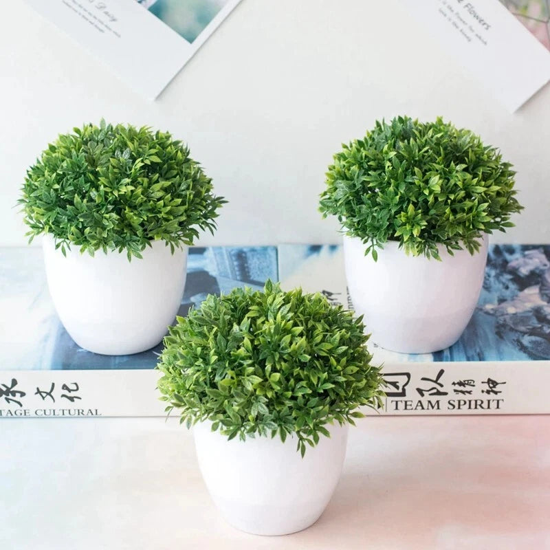 Set of three small artificial bonsai trees with green leafy tops in white pots