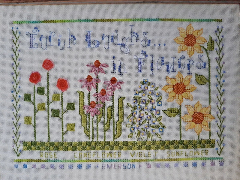 Floral cross-stitch pattern with roses, violets, and sunflowers around lettering