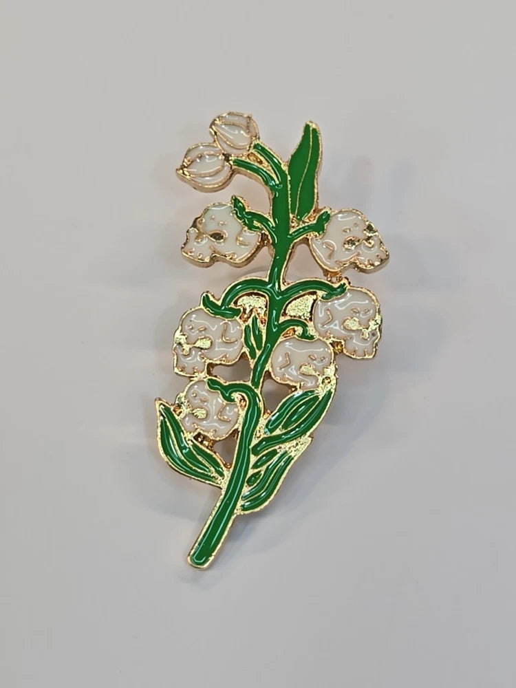 Skull and lily of the valley enamel lapel pin with green leaves and white flowers