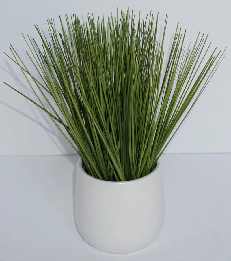 Artificial grass arrangement with upright green blades in a white planter pot