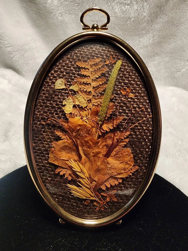 Oval domed glass dried flower frame with gold-tone border and pressed foliage