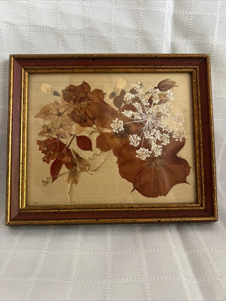Framed pressed flower and herb artwork with dried blooms and leaves in gold border