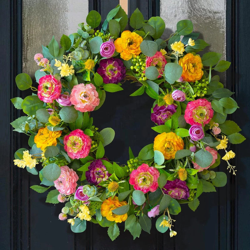 Outdoor spring wreath with pink, orange, yellow, and purple peony-style flowers and green leaves
