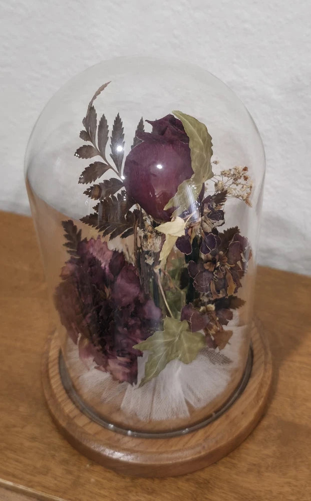 Glass dome with dried purple rose and assorted flowers on wood base