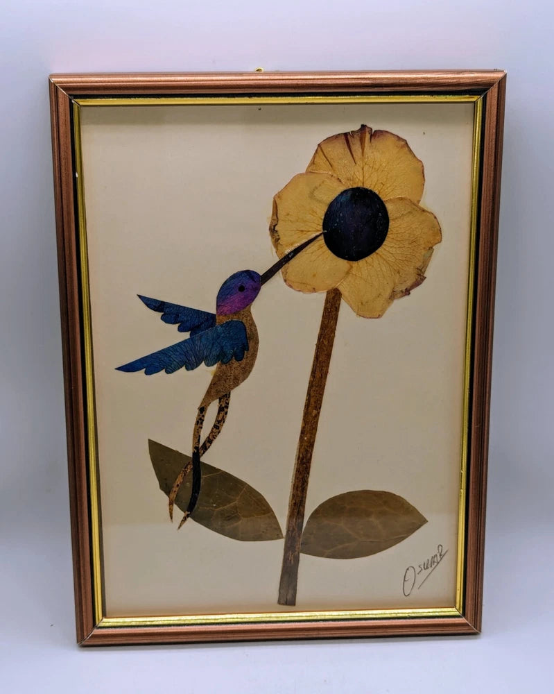 Framed pressed dried flower artwork with blue hummingbird, yellow bloom, and artist signature