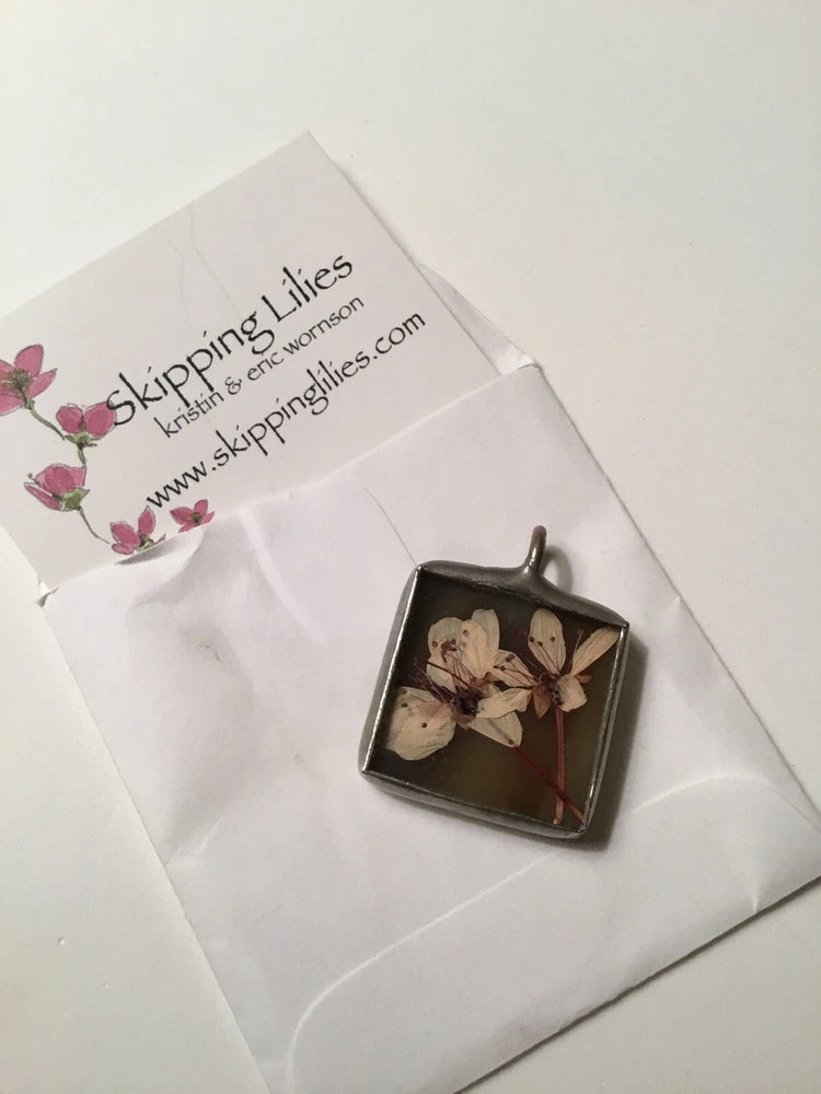 Pressed flower lily pendant with square resin bezel and dark metal loop bail