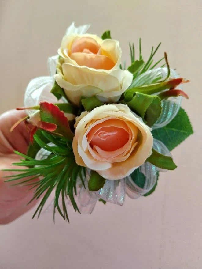 Rose wrist corsage bouquet with peach and cream roses, green leaves, and white ribbon