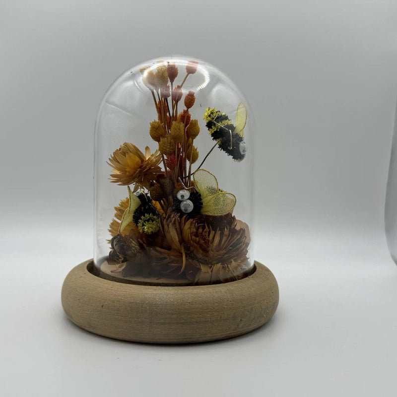 Glass dome on round wooden base with dried flowers and small bee ornament