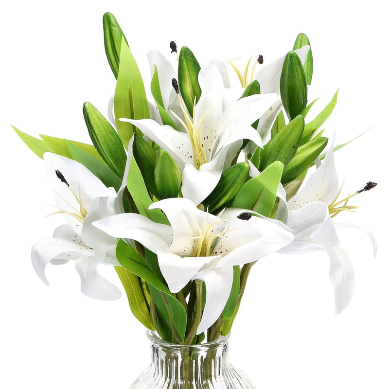 Artificial white lily flowers with green leaves, in clear glass vase