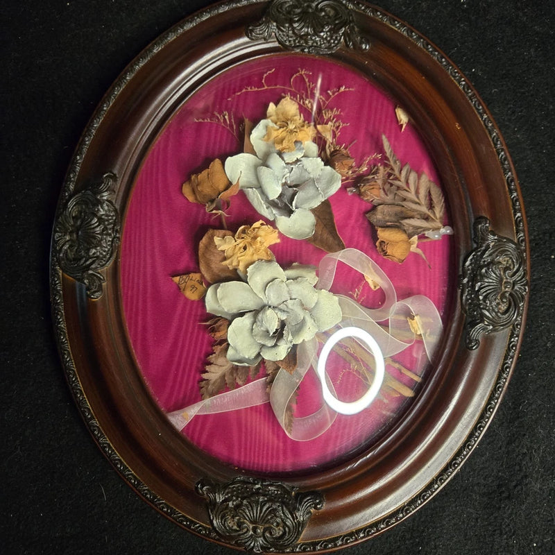 Oval concave frame with dried flowers and pale blooms on pink background