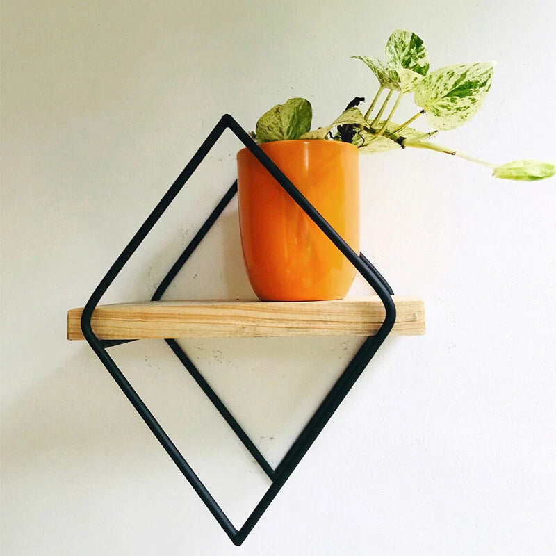 Diamond wall plant hanger with black metal frame and light wood shelf, holding an orange pot.