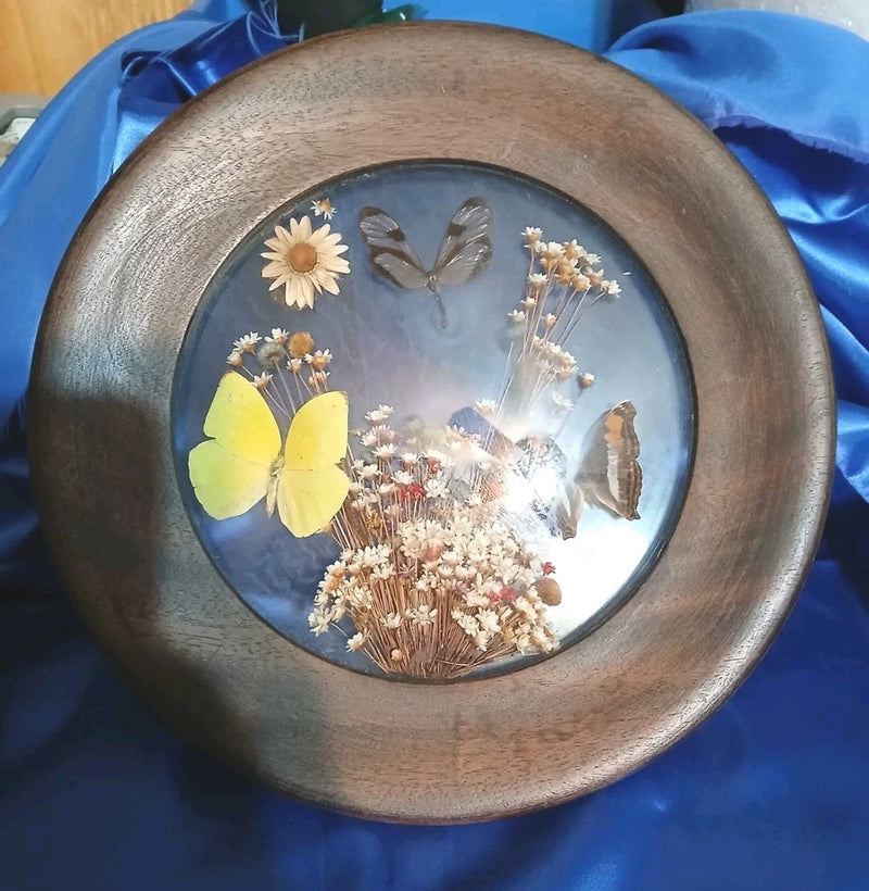 Round dried flower display with butterflies, yellow petals, and tan and white blooms in glass