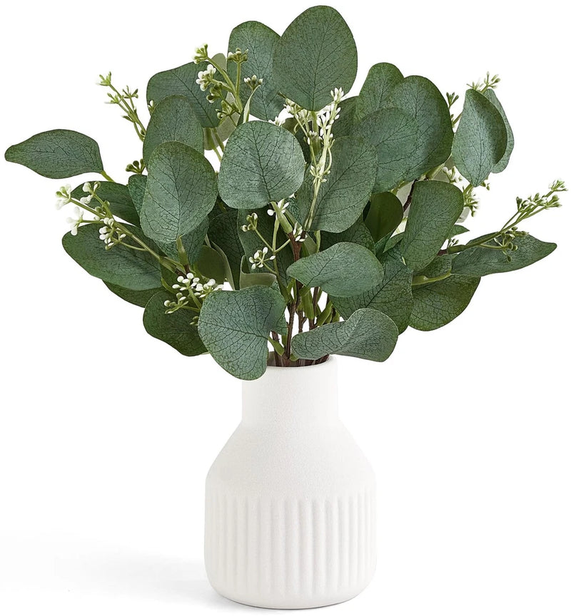 Artificial eucalyptus stems in small white ceramic vase with ribbed texture and green leaves