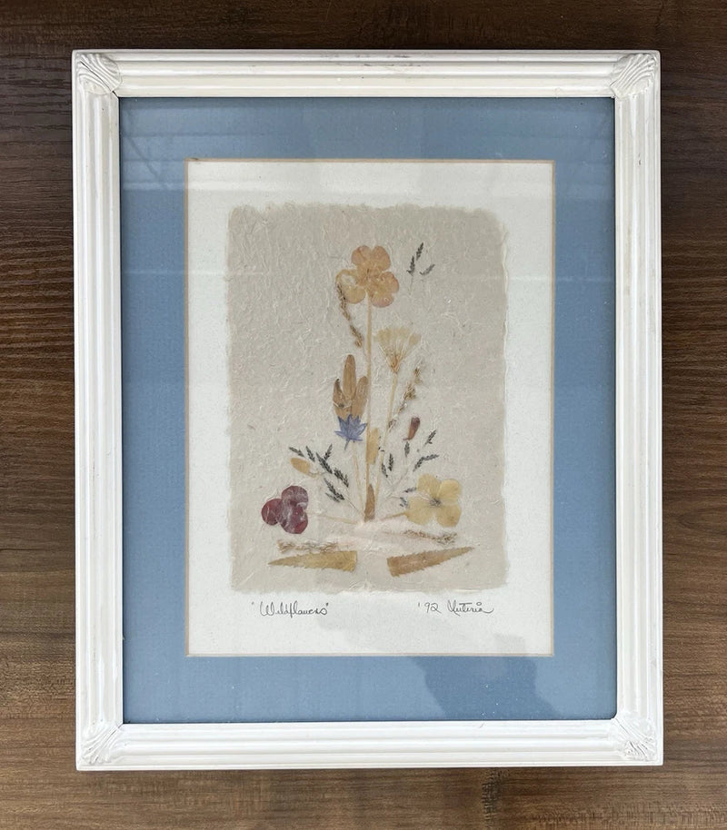 Framed pressed dried wildflower artwork with white frame and blue mat, mounted blossoms
