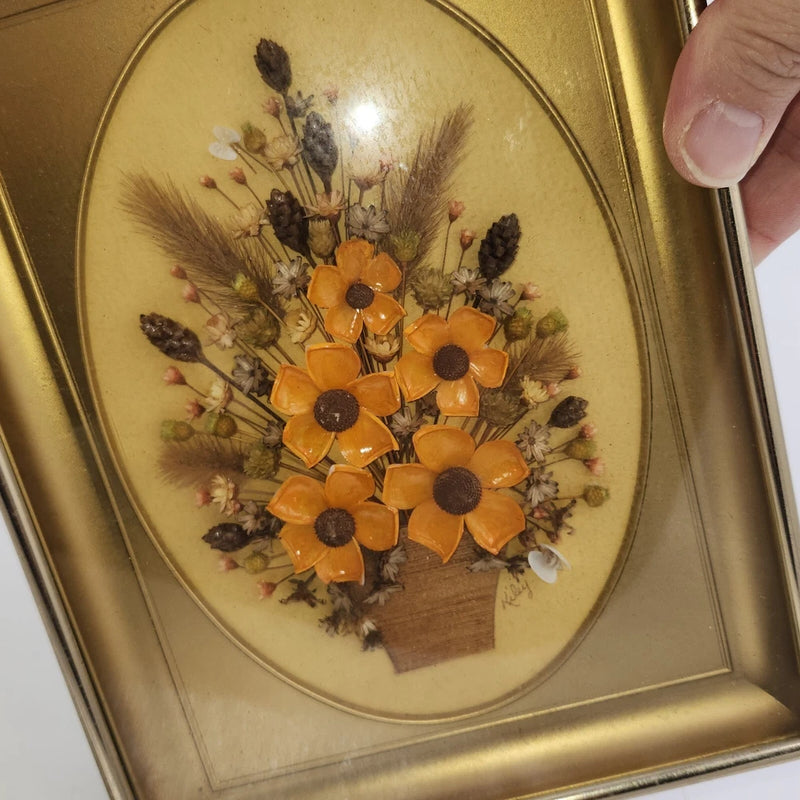 Oval framed pressed flower art with orange dried blooms and dark foliage