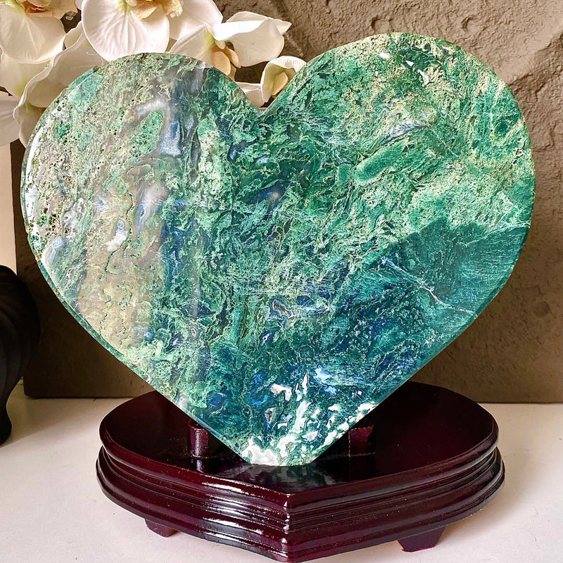 Heart-shaped green crystal specimen with marbled texture on dark wooden stand