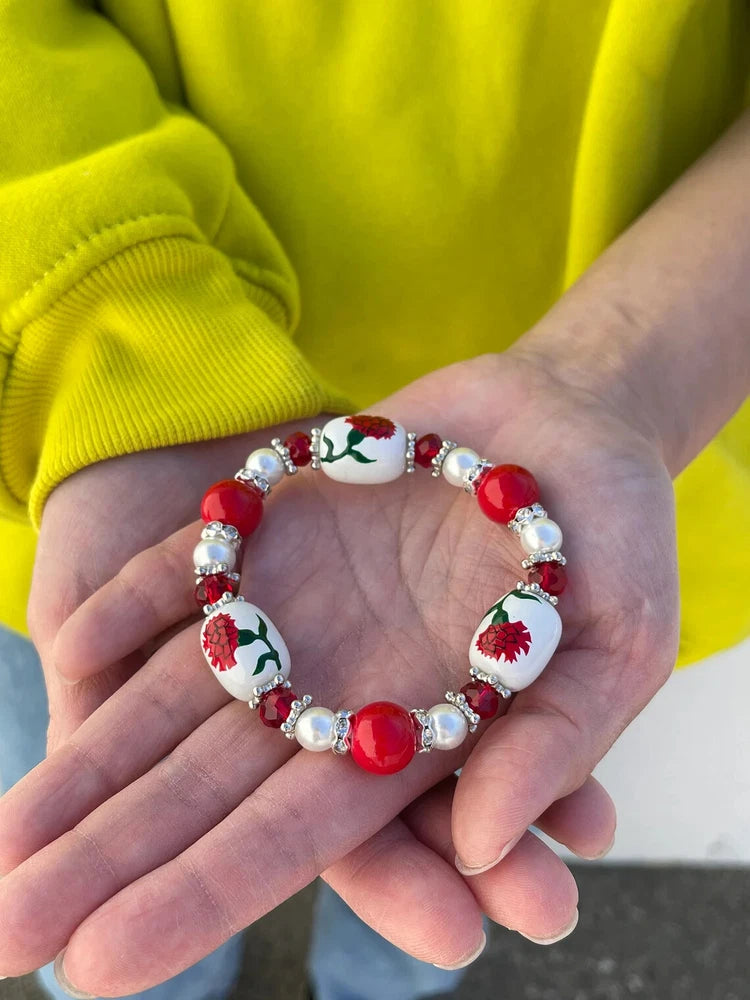 Floral bead bracelet with red and white flowers, green leaf accents, and crystal-like spacers