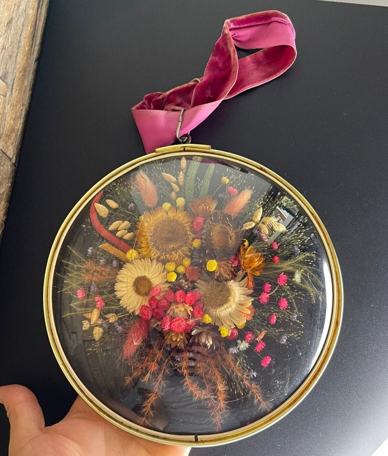 Round domed glass wall art with gold-tone frame and preserved dried flower bouquet