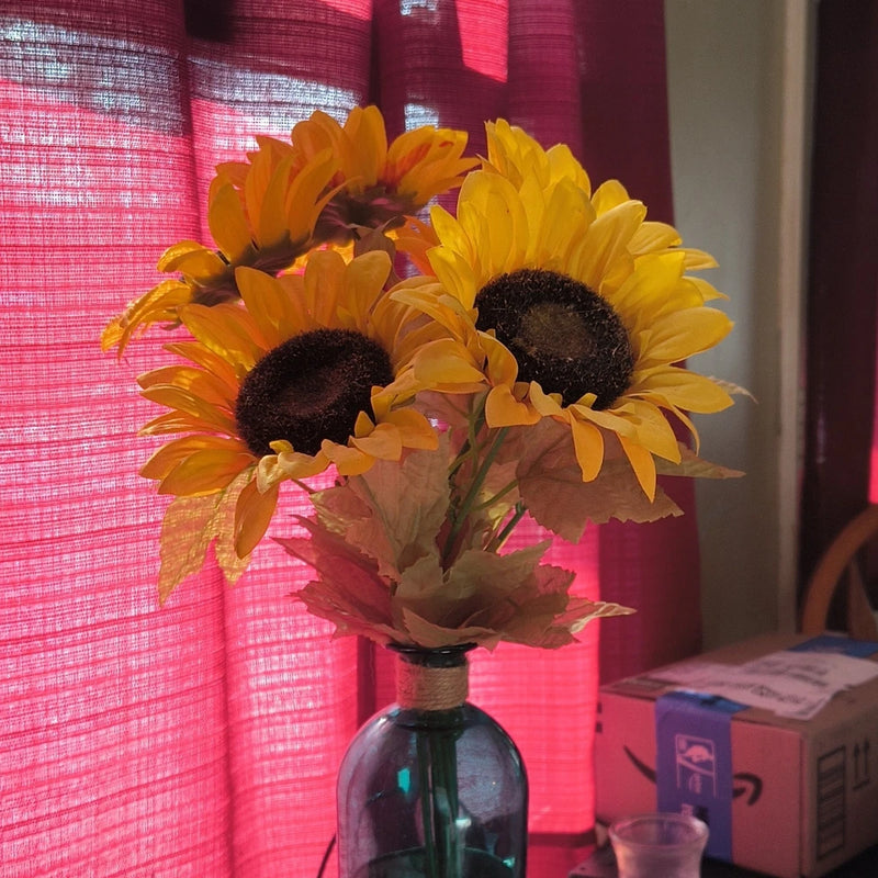 Artificial sunflower arrangement in blue glass vase with orange ribbon