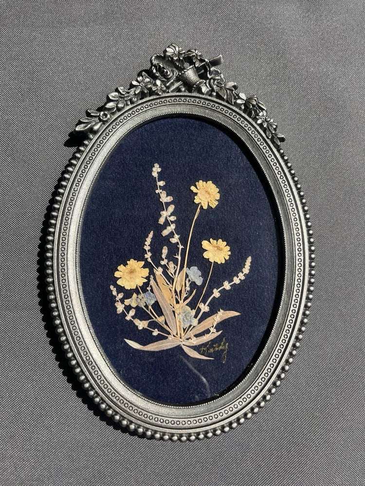 Oval framed pressed flower arrangement with yellow blooms on dark blue background
